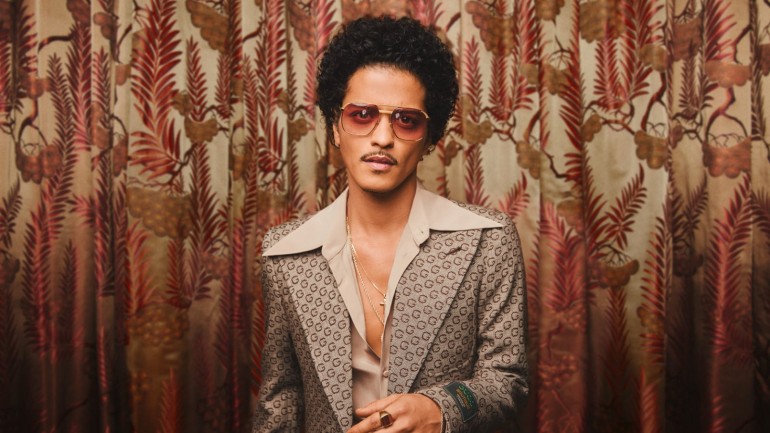 Der Sänger Bruno Mars steht in einem Anzug vor einem gemustertem Vorhang
